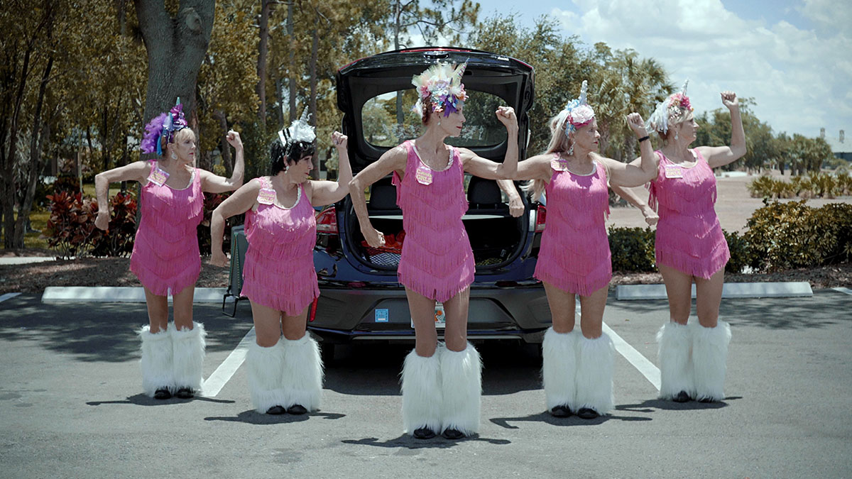 Ur filmen Calendar Girls. Syntolkning: Fem äldre kvinnor i rosa danskläder står uppställda i en dansformation på en parkeringsplats. Foto: Love Martinsen.