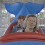 Syntolkning: Två äldre damer åker i en valformad karusellvagn.