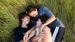 Tre glada systrar kramar om varandra i gräset.
