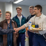 Syntolkning: David Dencik som Lars Norén skakar hand med internerna i ett kontorsrum.