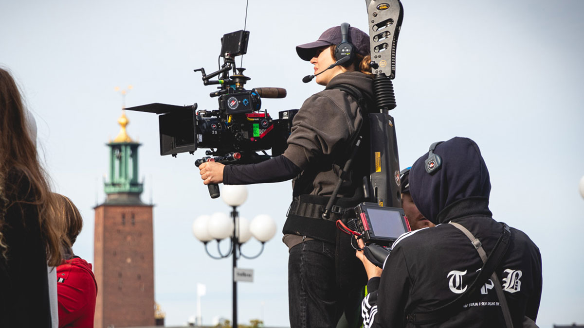 Filmfotograf med filmkamera. I bakgrunden syns Stockholms stadshus.