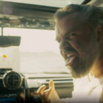 Närbild på man som sitter i passagerarsätet på en bil och räcker ut tungan.