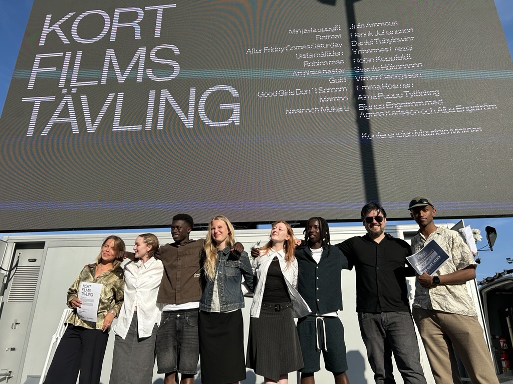 Gruppbild på uppradade personer framför en skärm med texten 