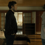 Tv män står efter varandra i en lägenhet och tittar åt höger utanför bildkant.