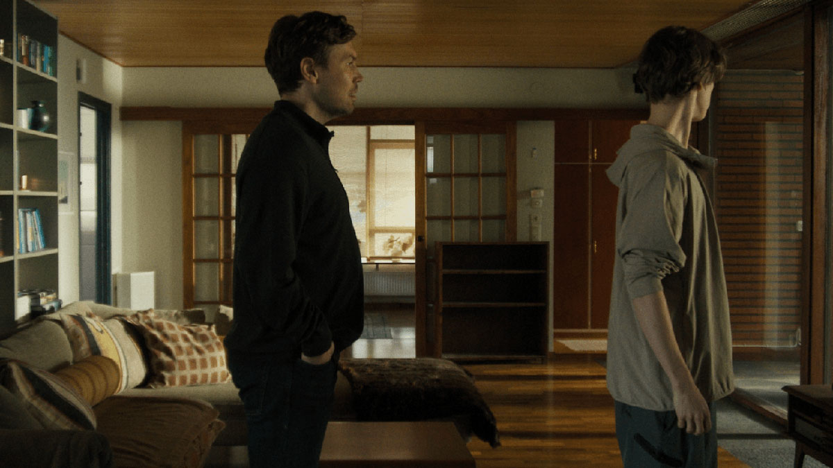 Tv män står efter varandra i en lägenhet och tittar åt höger utanför bildkant.