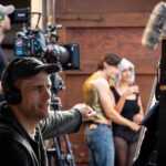 Regissör tittar på monitor medan en kamera i bakgrunden filmar två skådespelare.