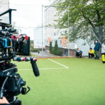 Filmkamera riktad mot tre skådespelare på en fotbollsplan.