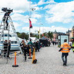 Filmkamera på ett högt stativ med Strandvägen i Stockholm i bakgrunden.