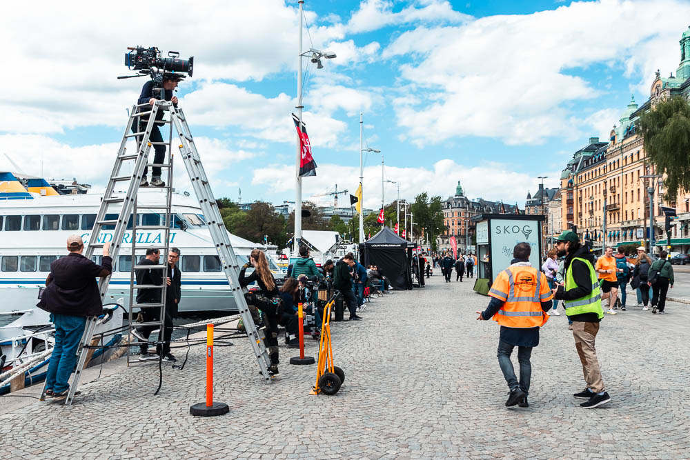 Filmkamera på ett högt stativ med Strandvägen i Stockholm i bakgrunden.