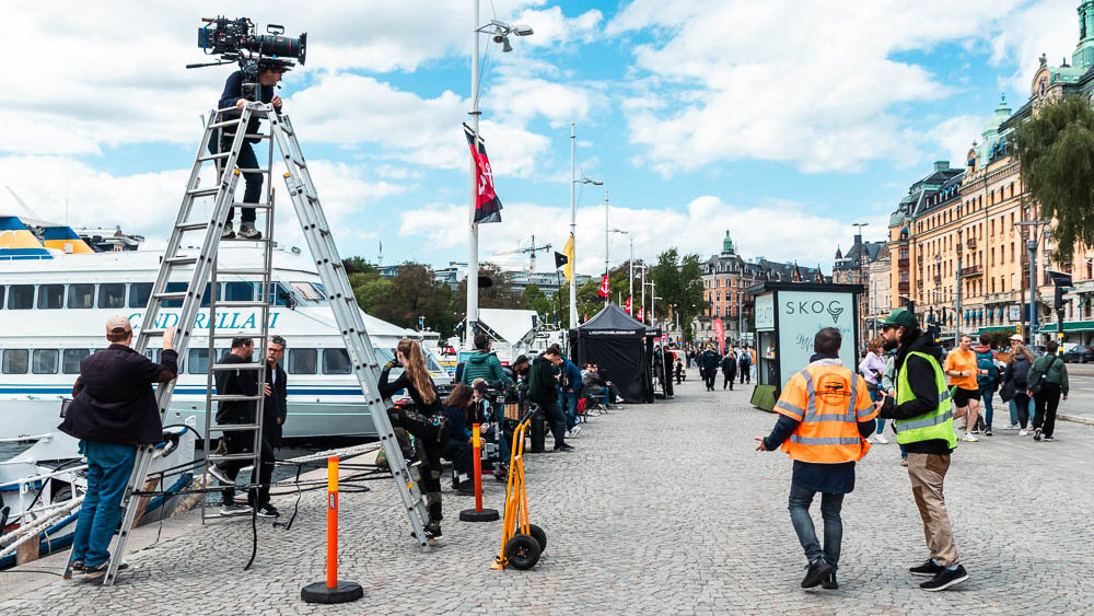 Filmkamera på ett högt stativ med Strandvägen i Stockholm i bakgrunden.