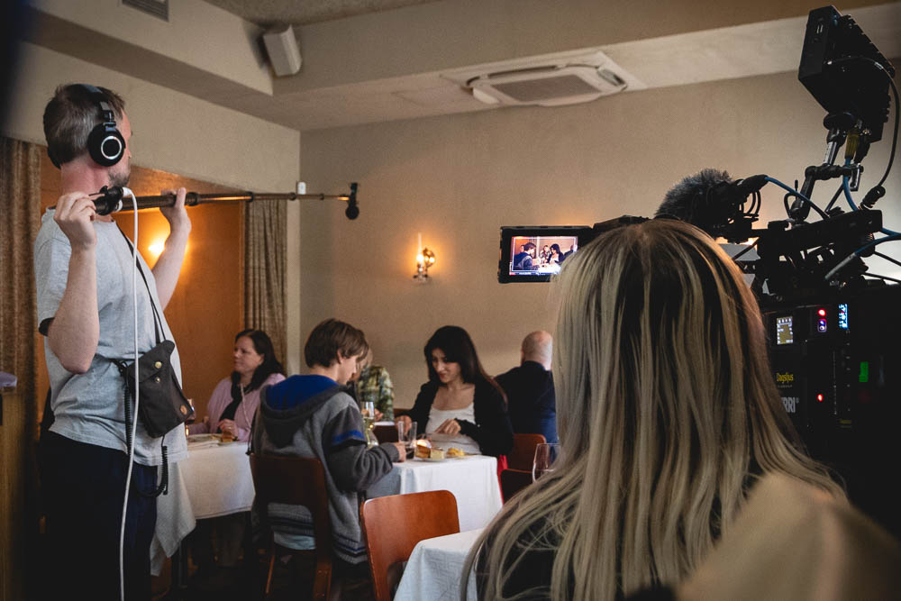 Filmteam arbetar runt ett par som sitter vid ett restaurangbord.