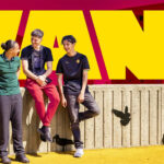 Tre killar vid en mur med texten 