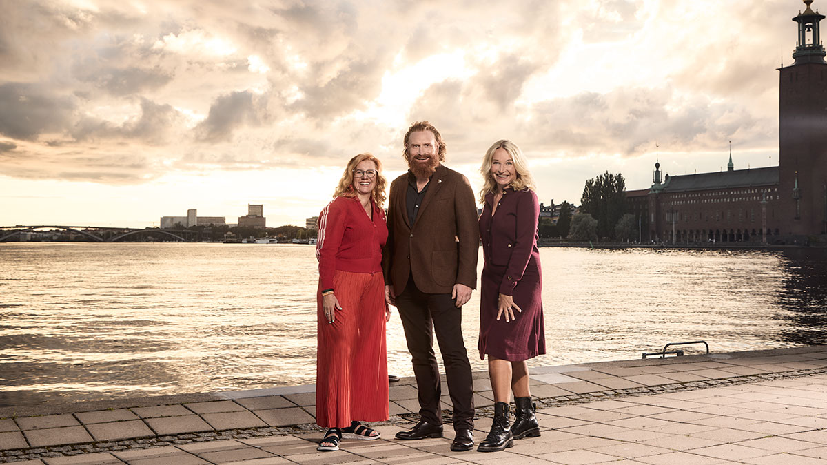 Gruppbild på två stående kvinnor och en man med Stockholms stadshus i bakgrunden.