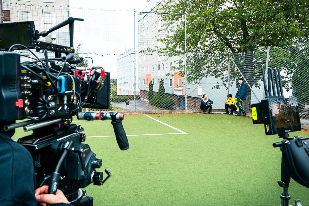 Filmkamera riktad mot tre skådespelare på en fotbollsplan.