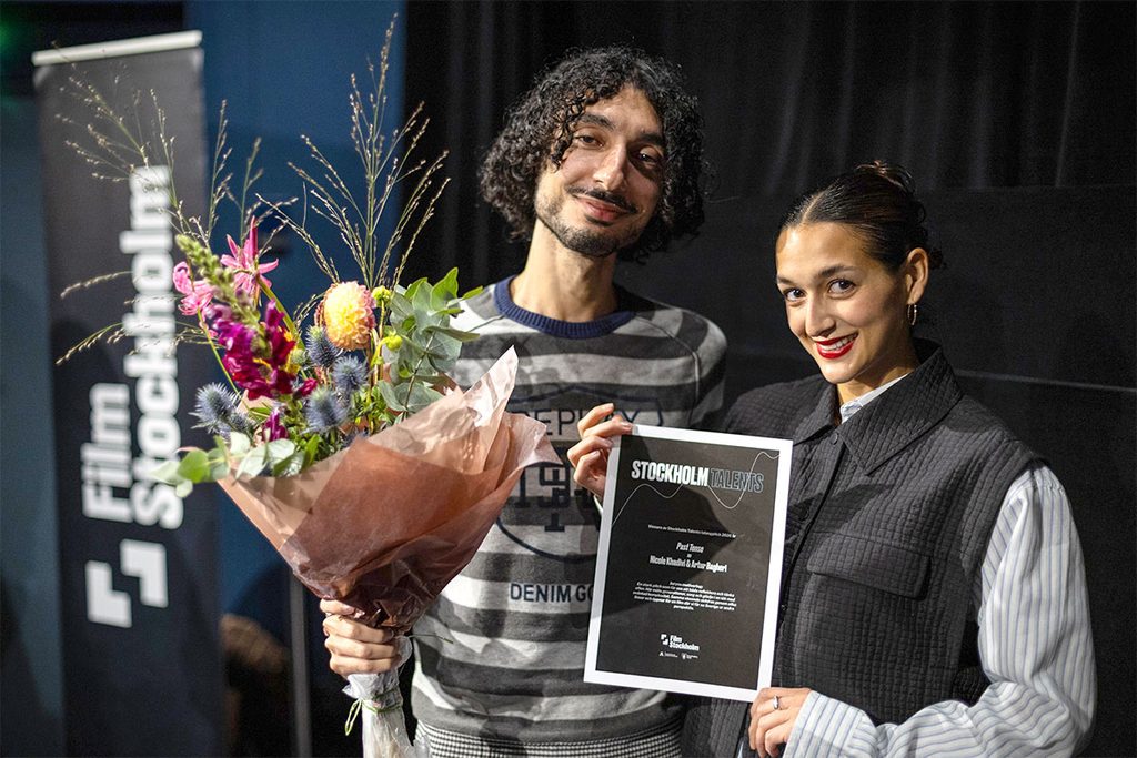 Två glada personer med diplom och blombukett.